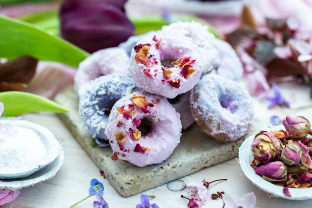 甜甜圈高角度拍摄一些蓝色和紫色的素食甜甜圈周围的鲜花在一张桌子上美味糕点背景