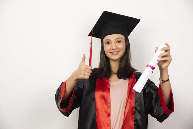 长袍刚毕业的女性 文凭 在白色背景下竖起大拇指成功女性毕业