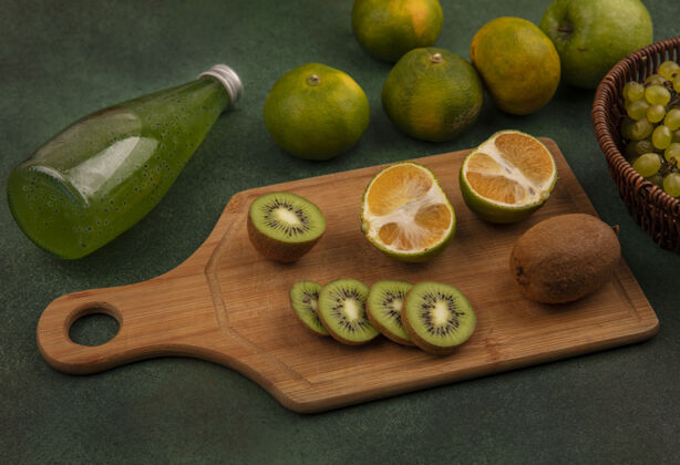 视野侧视图猕猴桃片在砧板上 橘子和一瓶果汁放在绿色的墙上果汁新鲜橘子