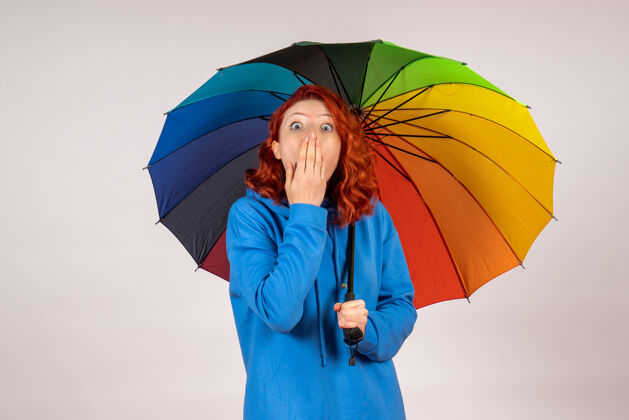 年轻女性白色墙壁上的年轻女性带着五颜六色的雨伞的正面视图庇护所保护封面彩虹
