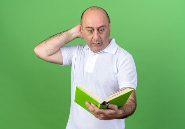 男人一个偶然的成熟男人拿着书 看着书 把手放在脑后 孤立在绿色的墙上抱头惊喜