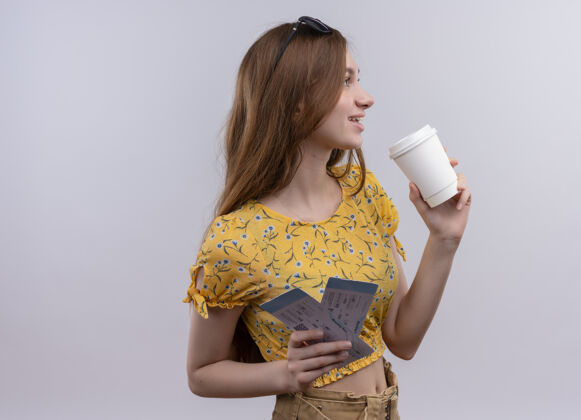 侧线微笑的年轻旅行家女孩拿着飞机票和塑料咖啡杯 看着右边的白色隔离墙和复印空间飞机拿着杯子