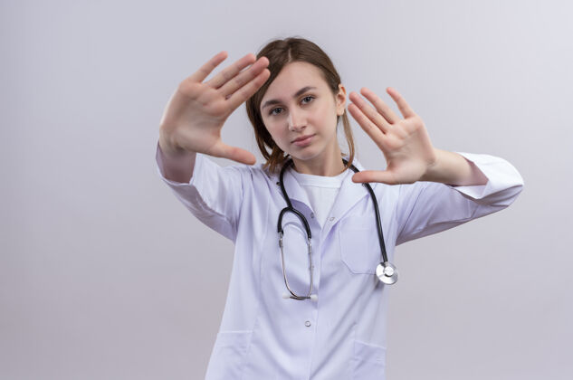 穿不幸的年轻女医生穿着医用长袍和听诊器在隔离的白色墙壁上做停止手势 并留有复印空间长袍医学年轻
