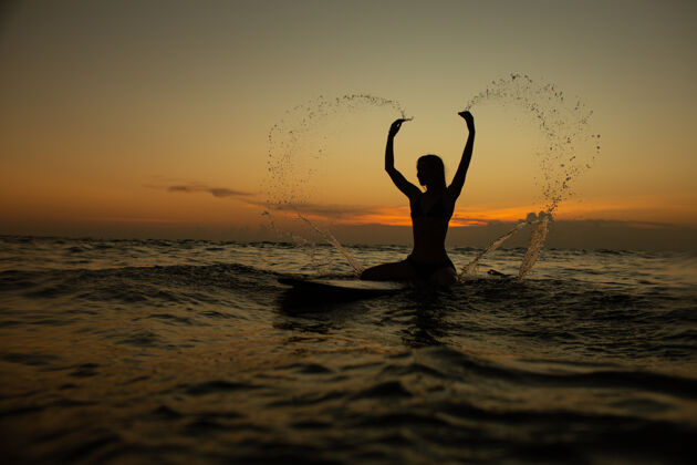 性感美丽的女孩在日落时拿着冲浪板沙滩地平线印度尼西亚