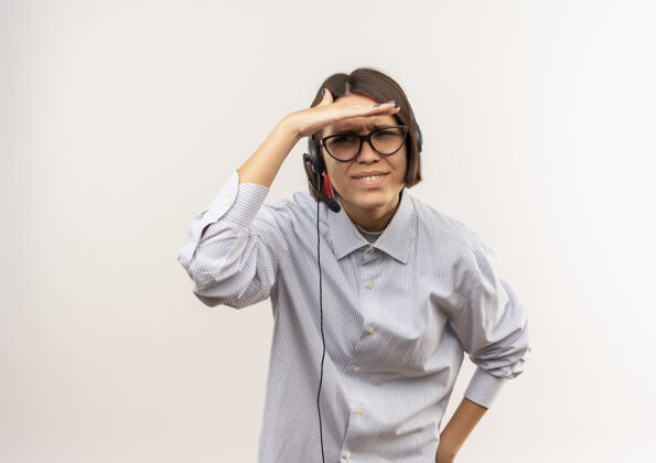空间困惑的年轻呼叫中心女孩戴着眼镜 戴着耳机 手靠近额头 看着远处隔离的白色带着复印空间眼镜耳机靠近