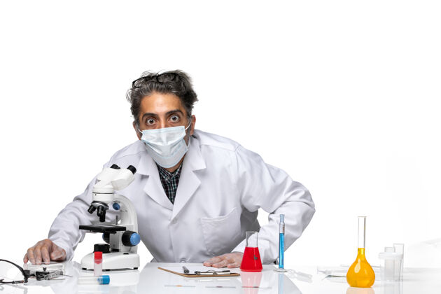 医学前视图中年科学家穿着特殊的白色西装使用显微镜使用科学外套