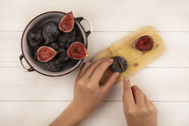 无花果俯视图中的女性手切割新鲜甜美的黑色无花果在木制厨房板上用刀在白色木墙上食物女性新鲜