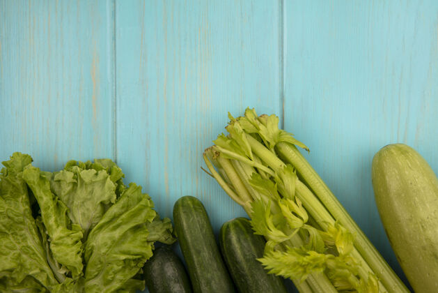 食品绿色蔬菜的俯视图 如黄瓜 莴苣 西葫芦和芹菜 隔离在蓝色的木墙上 留有复制空间观点生菜西葫芦