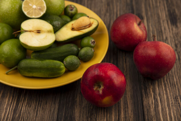 新鲜顶视图新鲜的红苹果和新鲜的水果 如青苹果 酸橙和鳄梨在一个黄色的盘子上的木制墙壁景观水果木材