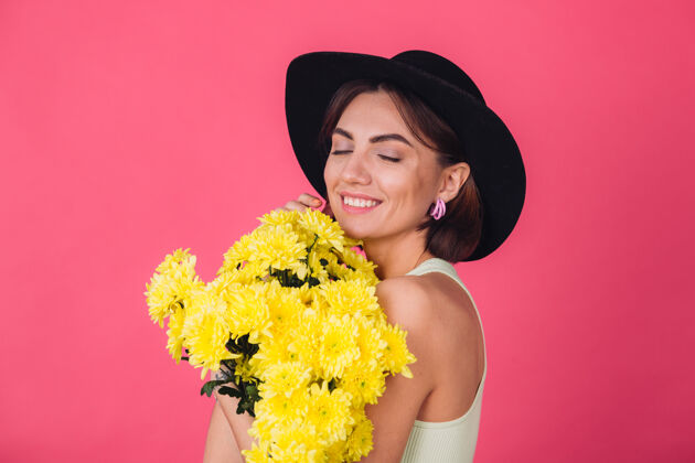 花时尚的女人戴着帽子 拥抱着一大束黄紫苑 春意盎然 快乐的情感与世隔绝的空间闭上眼睛肖像长深色