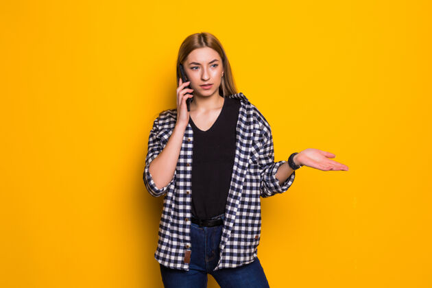 姿势困惑的年轻胖女人孤立地站在黄色的墙上 讲着手机肖像使用女人