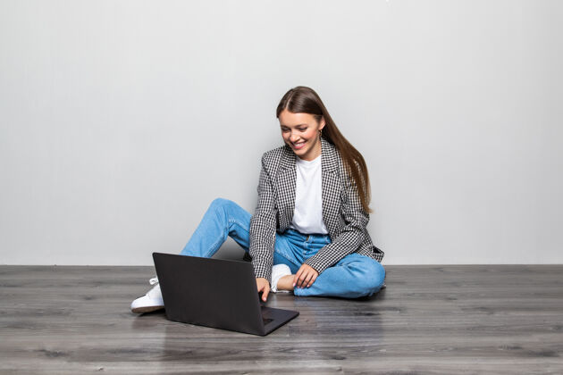 在线微笑的女人坐在地板上用笔记本电脑打字 两腿交叉自由职业者地板女性