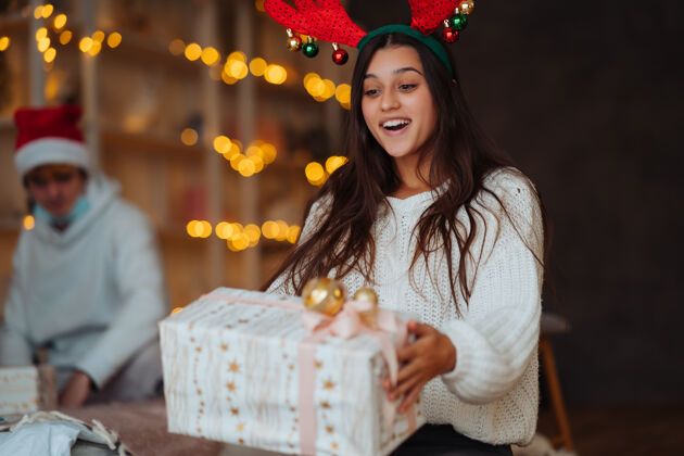 圣诞节有鹿角的年轻女子打开圣诞礼盒灯惊人鹿角
