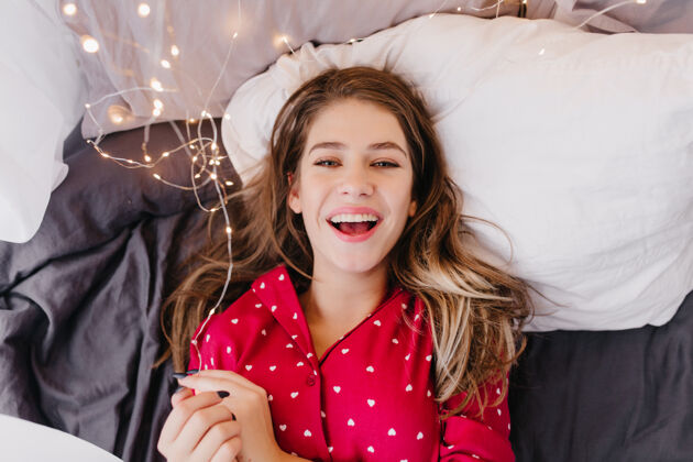 床幸福的欧洲女人穿着红色睡衣躺在黑色床单上情绪化的黑发女孩在床上笑的室内照片睡眠室内年轻
