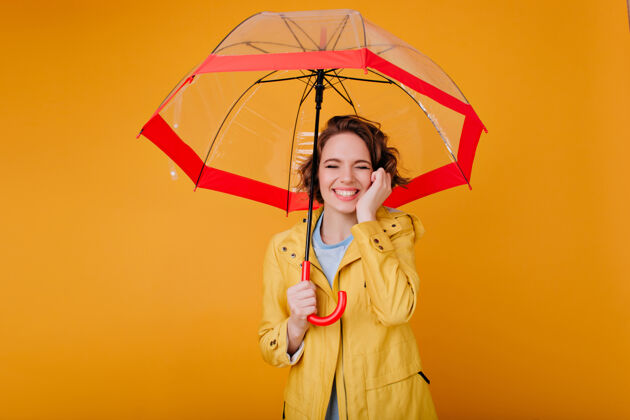 雨美丽的苍白女孩 穿着秋大衣 在阳伞下闭着眼睛微笑时尚的高加索女人 卷发 打着红伞配件外套肖像