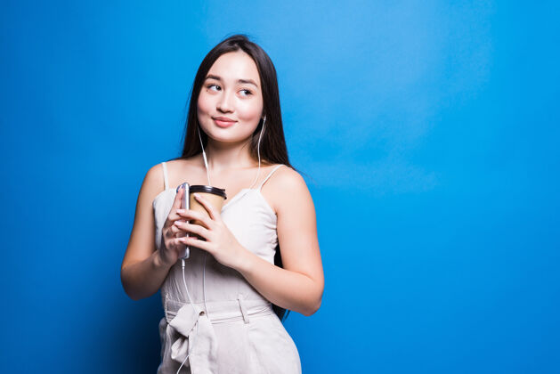 韩国人微笑着拿着外卖咖啡杯的亚洲年轻女子孤零零地站在蓝色的墙上女性美女美女