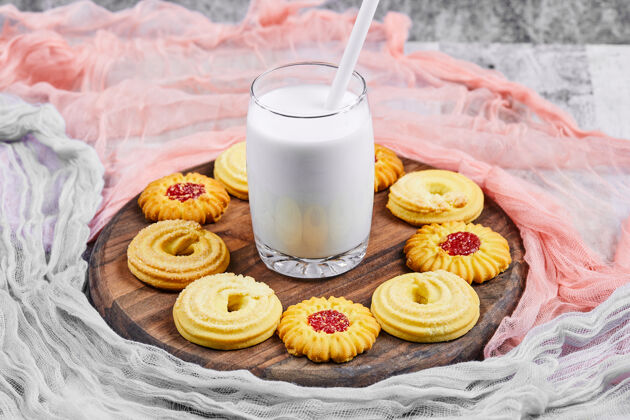 美味各种饼干和一罐牛奶放在一个木制盘子里 上面放着桌布甜点招待面包房