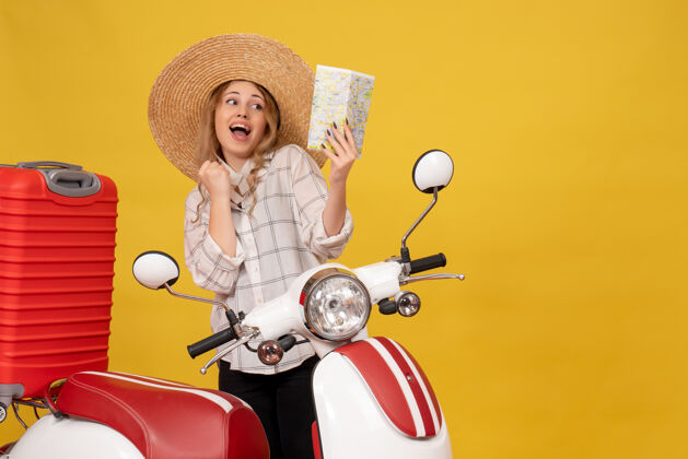 摩托车俯视图微笑的年轻女子戴着帽子 坐在摩托车上拿着地图 收拾行李行李收藏地图