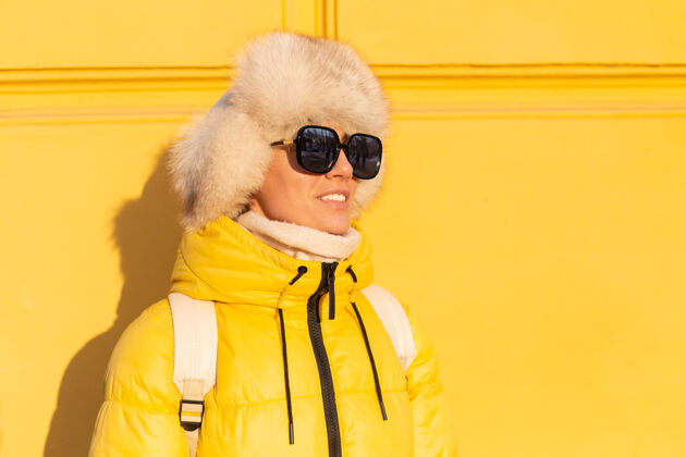 冷在阳光明媚的日子里 一个戴着温暖的俄罗斯西伯利亚帽子的快乐女人的肖像画 她在冬天穿着雪白的zabas 对着黄色的墙壁微笑着成人情感自拍
