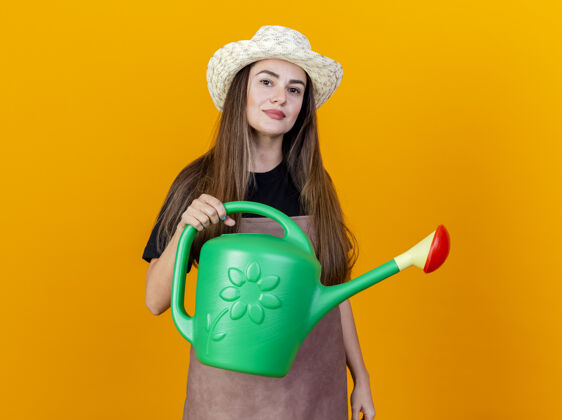 浇水高兴美丽的园丁女孩穿着制服和园艺帽举行浇水可以孤立在橙色的背景帽子举行制服