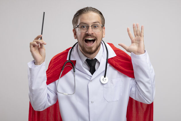 小伙子兴奋的年轻超级英雄穿着医用长袍 戴着听诊器和眼镜 举着白色背景的铅笔听诊器眼镜升起