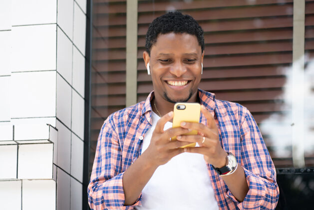 城市坐在街上商店橱窗边用手机的非裔美国人城市概念肖像男性快乐