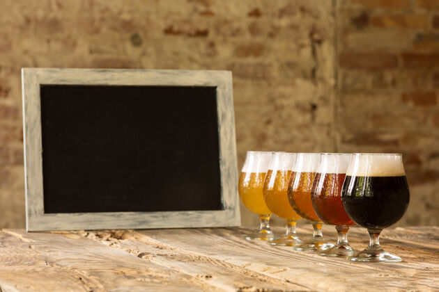 啤酒厂木桌上摆着不同种类的黑啤酒和淡啤酒 排成一行 黑板上摆着啤酒品脱冷