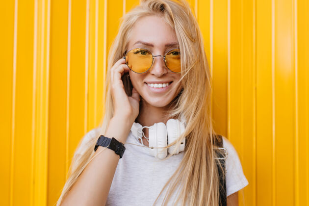 模特迷人的年轻女士在黄色背景上摆出美丽微笑的特写照片戴着耳机的快乐长发女孩表达着快乐的情绪情感积极休闲