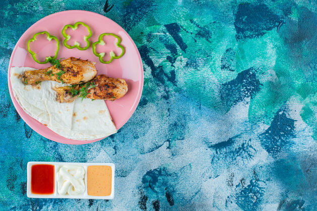 美味拉瓦什 烤鸡腿和胡椒粉放在盘子里 靠近酱汁碗 在蓝色背景上拉瓦什美味盘子