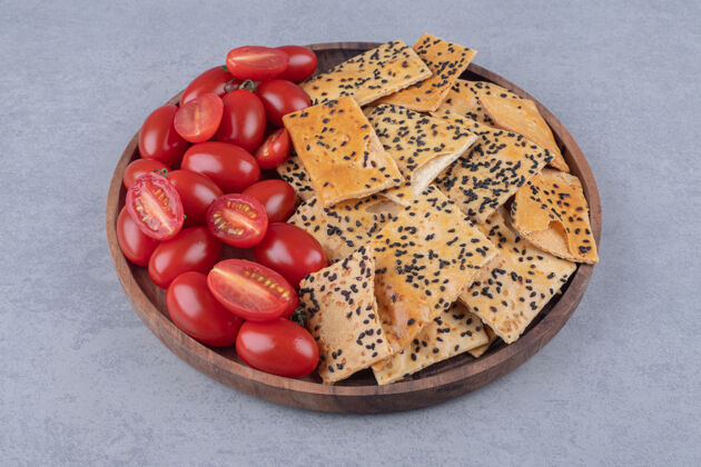 外套芝麻面包和番茄片堆在大理石桌上的木制托盘上美味有机面包