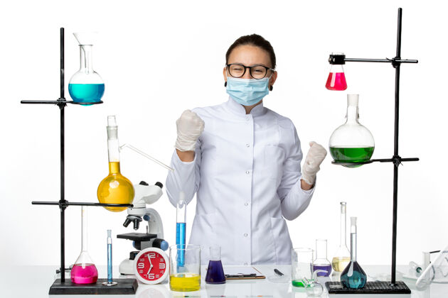 办公桌正面图：穿着医疗服的女化学家 戴着面罩 在白色办公桌上工作 病毒化学实验室 covidsplash前台科学病毒