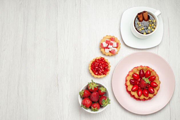草莓俯瞰白色书桌上的奶油蛋糕和一杯茶多汁小奶油蛋糕浆果