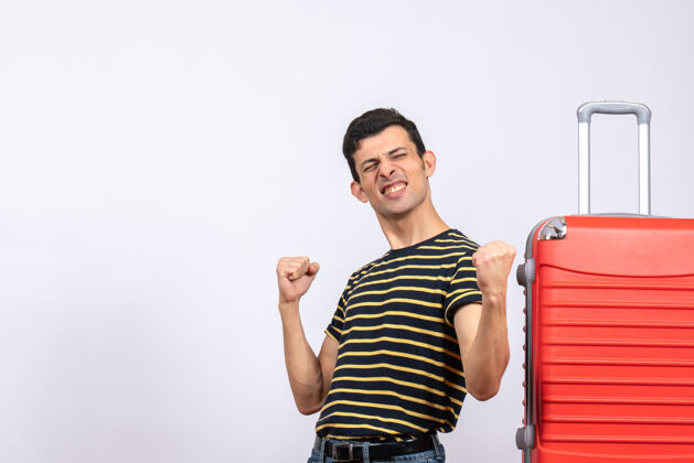 男性正面图：穿着条纹t恤和红色手提箱的欣喜若狂的年轻人手提箱快乐工作室