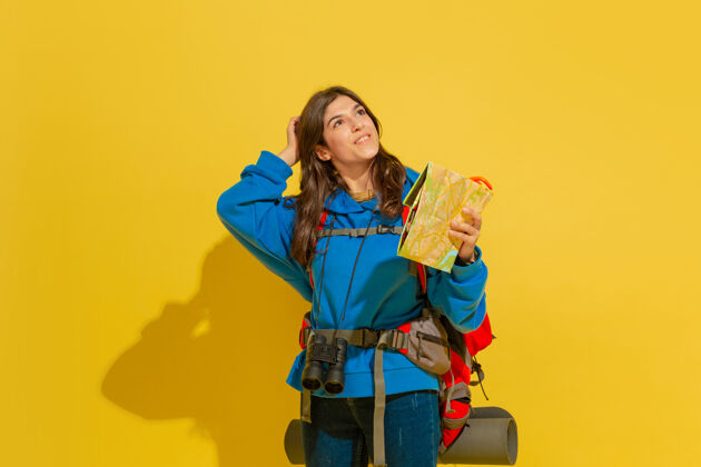 快乐一个快乐的年轻白人旅游女孩的肖像 带着包和望远镜 隔离在黄色的工作室背景上肖像旅游背景