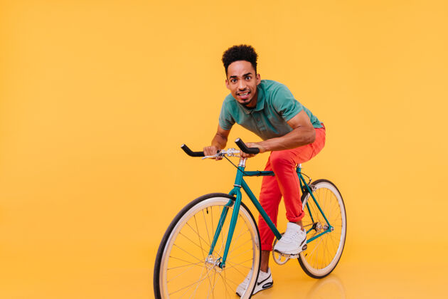 表情一个穿着红裤子的非洲男人骑着自行车有趣的黑人年轻人坐在自行车上的室内照片人放松家伙