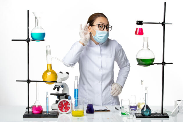 专业前视图穿着医疗服的女化学家戴着面具试图听到白色背景上的病毒化学实验室的病毒-飞溅视图实验室外套