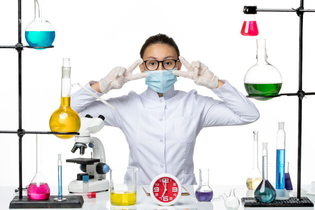 坐姿前视图穿着医疗服的女化学家带着面罩坐在白色背景上的溶液化学病毒-喷溅面罩化学药