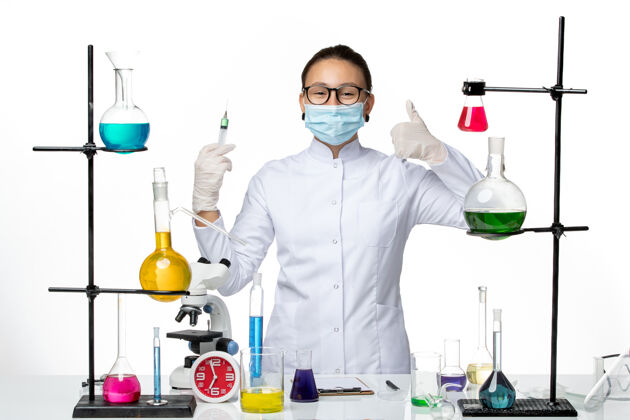 喷溅前视图身穿医疗服的女化学家 戴着面罩 在浅白色背景上注射病毒化学实验室的covidsplash套装面罩外套
