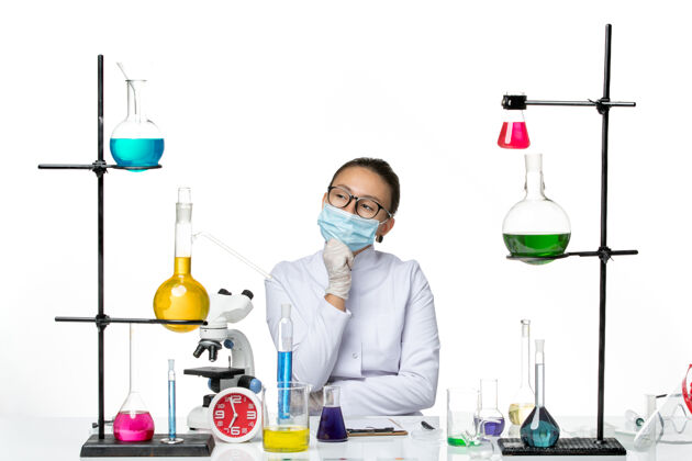 科学前视图穿着医疗服的女化学家带着面罩坐在桌子前思考白色背景病毒化学实验室的病毒飞溅坐面具前面