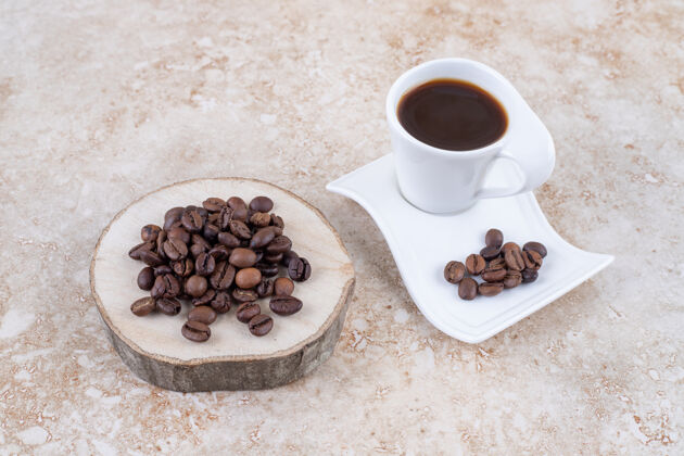 堆咖啡豆放在木板上 盘子旁边放着一杯煮好的咖啡咖啡豆