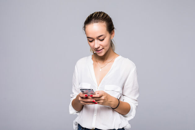 女士美丽微笑的女孩站在灰色的墙上用智能手机打短信的特写照片牙关成功人士企业家