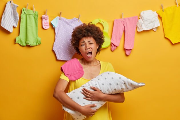深情疲惫的母亲打哈欠想睡觉 抱着裹在毯子里的新生婴儿摆姿势 厌倦了做家务 有很多工作要做 就像关心婴儿一样为人父母 疲倦和孤独睡眠新生儿衣服