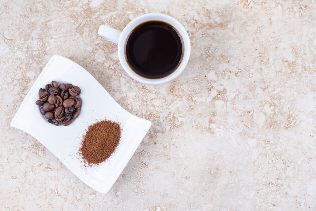 咖啡盘一杯煮好的咖啡 旁边放着咖啡豆和磨碎的咖啡粉 放在一个漂亮的盘子里咖啡美味芳香
