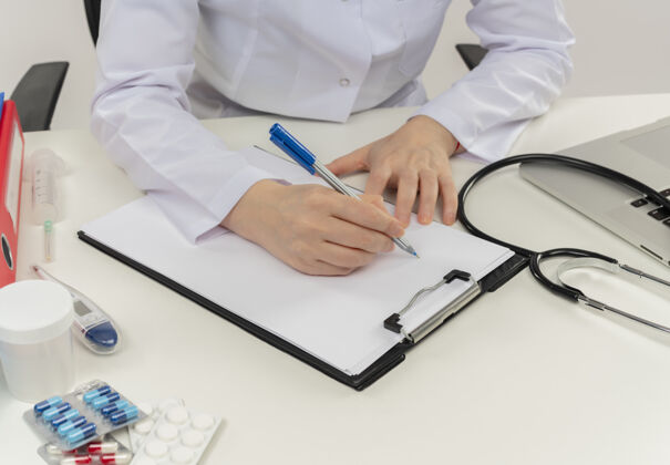 人一张女医生手拿着医疗工具和笔记本电脑在写字台上写处方的剪贴照片镜头笔记本电脑女人