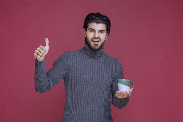 人穿着灰色毛衣的男人拿着咖啡杯 享受着咖啡的味道冬天热工人