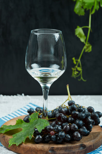 黑的一盘带叶子的黑葡萄和一杯深色背景的葡萄酒高质量的照片木头大自然成熟