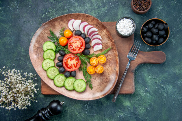 盘子俯瞰图新鲜切碎的蔬菜在棕色盘子上的木制砧板橄榄在碗盐大蒜素花上的混合色背景午餐板晚餐