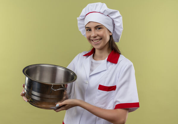 烹饪身着厨师制服的年轻高加索厨师女孩微笑着拿着锅 看着隔离在绿色背景上的相机 还有复印空间女孩微笑厨师