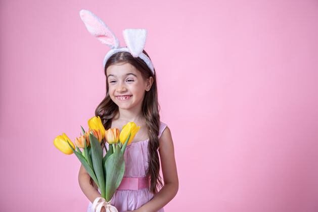 摄影棚带着复活节兔子耳朵的快乐小女孩微笑着 手里拿着一束郁金香 背景是粉色的工作室兔子郁金香孩子