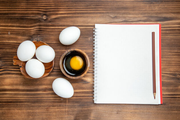 生的俯视整个生鸡蛋与记事本棕色木质表面膳食早餐木质鸡蛋鲍勃风景鸡蛋